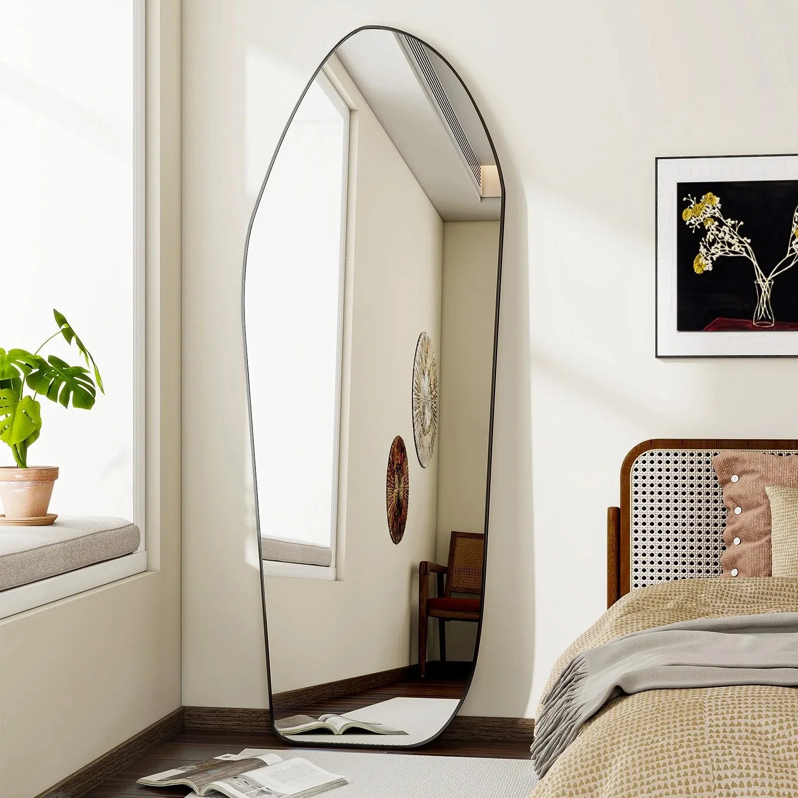 Large floor mirror in a bedroom with a bed, plant, and wall art.